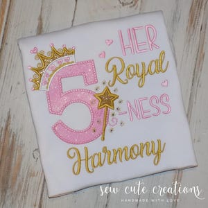 May include: White t-shirt with a pink glittery number 5, a gold crown, and a gold star wand. The text reads "HER Royal -NESS Harmony" in gold and pink. The shirt is decorated with hearts and stars.