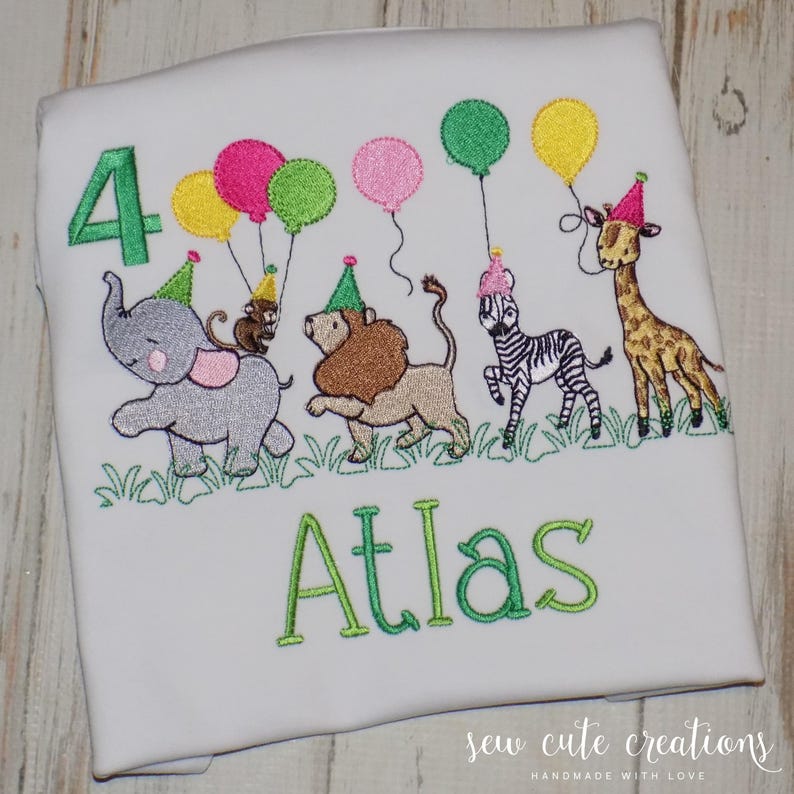Puede incluir: Una camiseta blanca con un dise&ntilde;o bordado que incluye el n&uacute;mero 4 en verde, el nombre Atlas en verde y un grupo de animales de safari como un elefante, mono, le&oacute;n, cebra y jirafa con gorros de fiesta y globos de colores.