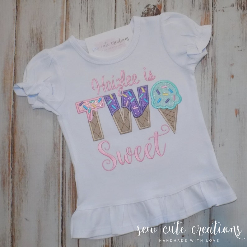 May include: White short-sleeved shirt with pink embroidery that says "Haizlee is TWO Sweet" with the number two designed as ice cream cones with sprinkles.