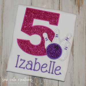 Puede incluir: Camiseta blanca con un gran número 5 rosa brillante. Debajo, el nombre "Izabelle" en morado. Un gráfico de bolos y bolos está a la derecha. El texto "sew cute creations" está en la parte inferior.