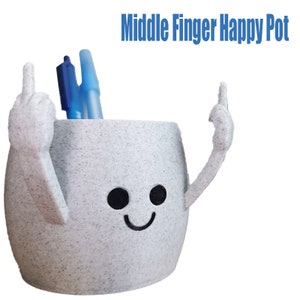May include: A grey speckled ceramic pot with a smiling face and two arms, each giving the middle finger. The pot contains blue pens and the text "Middle Finger Happy Pot" is above it. A humorous desk accessory.