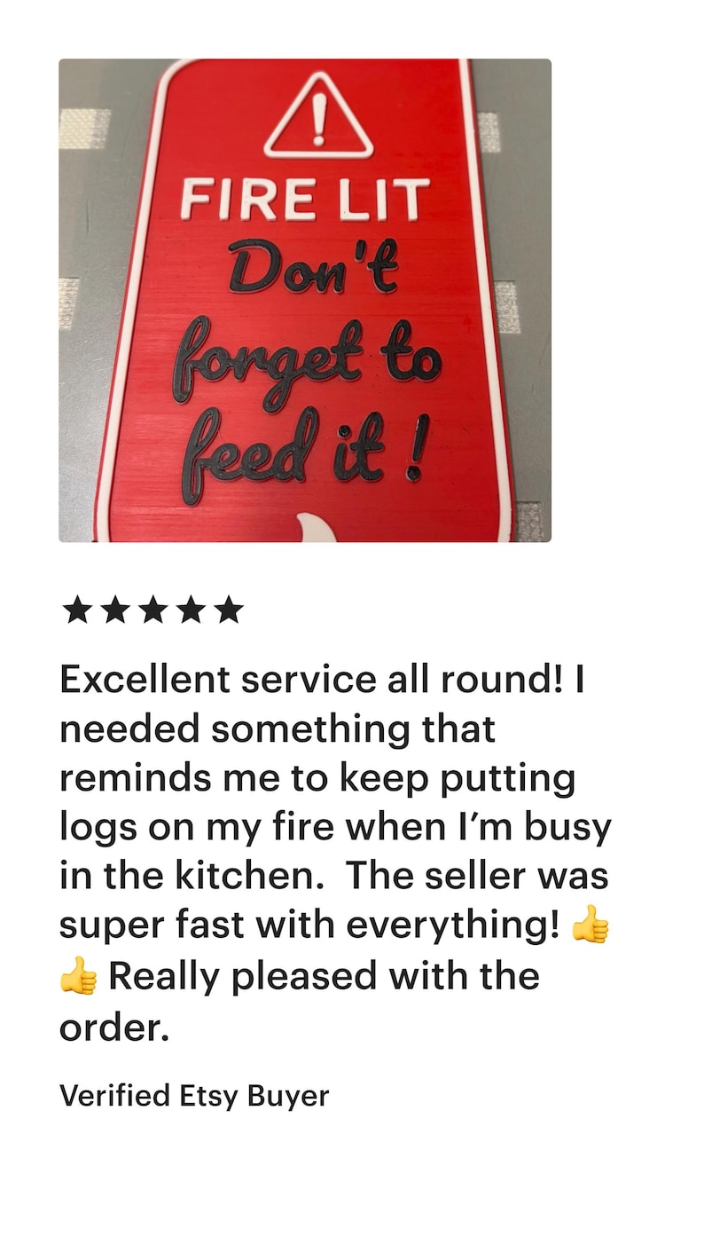 K&ouml;nnte beinhalten: Rotes rechteckiges Schild mit wei&szlig;em Rand und Text: "FIRE LIT Don't forget to feed it!" Mit einem wei&szlig;en Ausrufezeichen-Symbol. Das Schild erinnert daran, Holz ins Feuer zu legen.