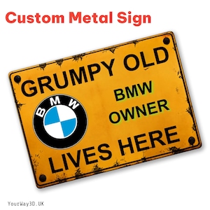 Op de afbeelding: Een rechthoekig geel metalen bord met zwarte tekst die luidt GRUMPY OLD BMW OWNER LIVES HERE. Het bord is voorzien van het ronde blauwe, witte en zwarte BMW-logo aan de linkerkant en heeft vier donkere montagegaten in de hoeken.