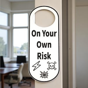 K&ouml;nnte beinhalten: Wei&szlig;er T&uuml;rh&auml;nger mit schwarzem Rand und dem Text "On Your Own Risk". Das Schild enth&auml;lt einen Blitz, Totenkopf und gekreuzte Knochen sowie eine Explosionsgrafik. Das Schild h&auml;ngt an einer beigen T&uuml;r.