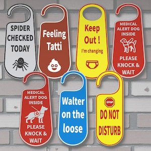 K&ouml;nnte beinhalten: Eine Sammlung von T&uuml;rschildern in verschiedenen Farben, jeweils mit einer einzigartigen Botschaft. Die Schilder enthalten S&auml;tze wie "Spider Checked Today", "Feeling Tatti" und "Do Not Disturb". Einige zeigen Illustrationen.
