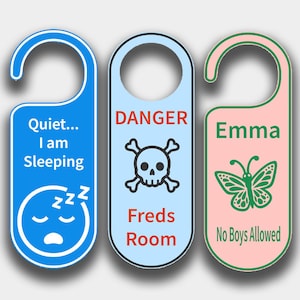 Op de afbeelding: Drie deurhangers met verschillende ontwerpen. De eerste is blauw met de tekst "Quiet... I am Sleeping" en een slapend gezicht. De tweede is lichtblauw met een schedel en gekruiste botten en de tekst "DANGER Freds Room". De derde is roze met een vlinder en de tekst "Emma No Boys Allowed".