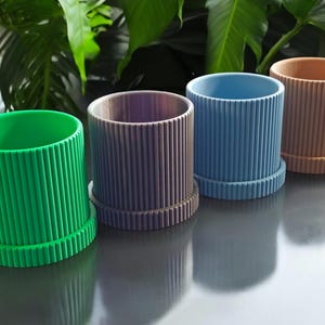 May include: Four different colored planter pots with a ribbed design. The pots are green, gray, blue, and brown.