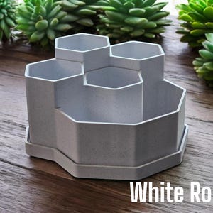 May include: A white hexagonal desk organiser with six compartments. The organiser is made of a textured material and has a base.
