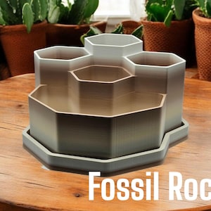 May include: A hexagonal-shaped desk organiser with six compartments, made of a light grey plastic with a gradient effect. The organiser is sitting on a wooden surface and the text "Fossil Rock" is printed below it.
