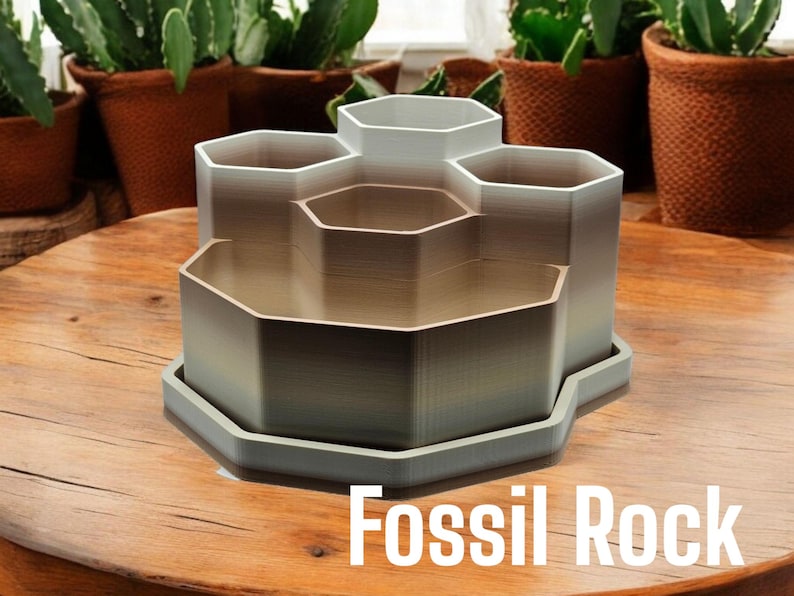 May include: A hexagonal-shaped desk organiser with six compartments, made of a light grey plastic with a gradient effect. The organiser is sitting on a wooden surface and the text "Fossil Rock" is printed below it.