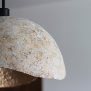 May include: A close-up of a beige, textured, dome-shaped lampshade with a black cord and a black metal fixture.