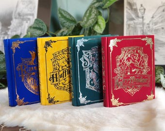 May include: Four hardcover books with different coloured covers and gold embossed crests. The books are titled "Ravenclaw", "Hufflepuff", "Slytherin", and "Gryffindor".