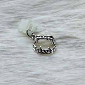 May include: Silver charm with a detailed design of a set of fangs. The charm is attached to a clear plastic clip.