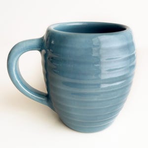 May include: A blue ceramic mug with a rounded body and a curved handle. The mug has a textured, ridged surface and a glossy finish. The mug is designed for hot beverages and is suitable for home or office use.