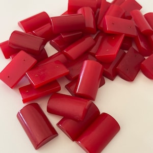 May include: A pile of red, rectangular and half-round shaped beads. The beads are made of a smooth, polished material.