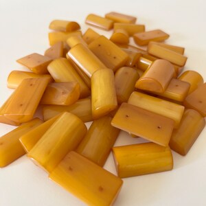 May include: A pile of amber-colored plastic buttons in various shapes and sizes. Some buttons are rectangular, while others are rounded. All buttons have two holes.