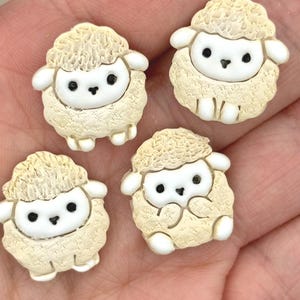 May include: Four small, flat-backed sheep figurines made of cream-coloured textured material. Each sheep has a smooth white face, two black eyes, and a small black nose. The woolly bodies feature a detailed, bumpy texture, and the small limbs are white.