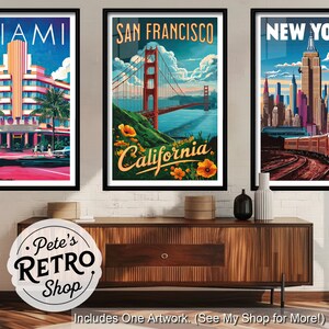 K&ouml;nnte beinhalten: Drei gerahmte Reiseplakate mit Stadtansichten. Die Plakate zeigen Miami, San Francisco und New York. Das San Francisco-Poster zeigt die Golden Gate Bridge. Die Plakate werden &uuml;ber einem Holzschrank ausgestellt.