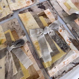 May include: Several fabric bundles with a patchwork design in shades of beige, brown, and yellow. Each bundle is tied with a gray ribbon bow. The fabric appears to be textured and possibly handmade, with a rustic aesthetic.