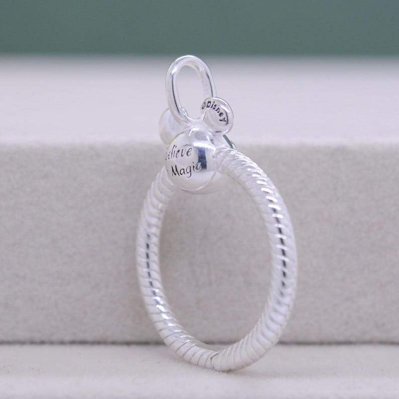 Pu&ograve; includere: Un charm argentato dal design circolare. Il charm presenta le parole "Believe Magic" e una piccola testa di Topolino. L'anello &egrave; strutturato con un motivo a spirale. Il charm ha un anello nella parte superiore per l'attacco.