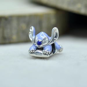 May include: A silver-toned metal charm featuring a light blue enameled character with large ears, a dark blue nose, and closed eyes, depicted in a resting position. The charm has a polished metallic finish and a detailed, sculpted design.