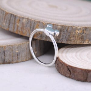 May include: A silver ring featuring a three-circle design, reminiscent of a famous cartoon character. The ring is set against a backdrop of wooden slices, highlighting its simple yet recognizable form. The ring's design is a playful and whimsical accessory.