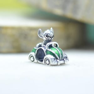 May include: A silver charm bead featuring a character with large ears sitting inside a small green and silver car. The metal surface is polished, and the car body is accented with green enamel detailing on the hood and sides of the vehicle.
