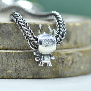 May include: A sterling silver charm featuring a character figure with antennae, threaded onto a braided silver chain. The back of the charm is engraved with the text PANDORA, S925 ALE, and Disney, indicating the brand, material, and licensing.