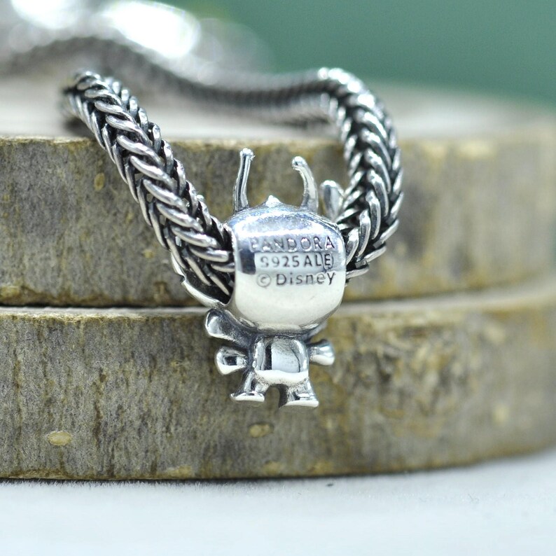 May include: A sterling silver charm featuring a character figure with antennae, threaded onto a braided silver chain. The back of the charm is engraved with the text PANDORA, S925 ALE, and Disney, indicating the brand, material, and licensing.