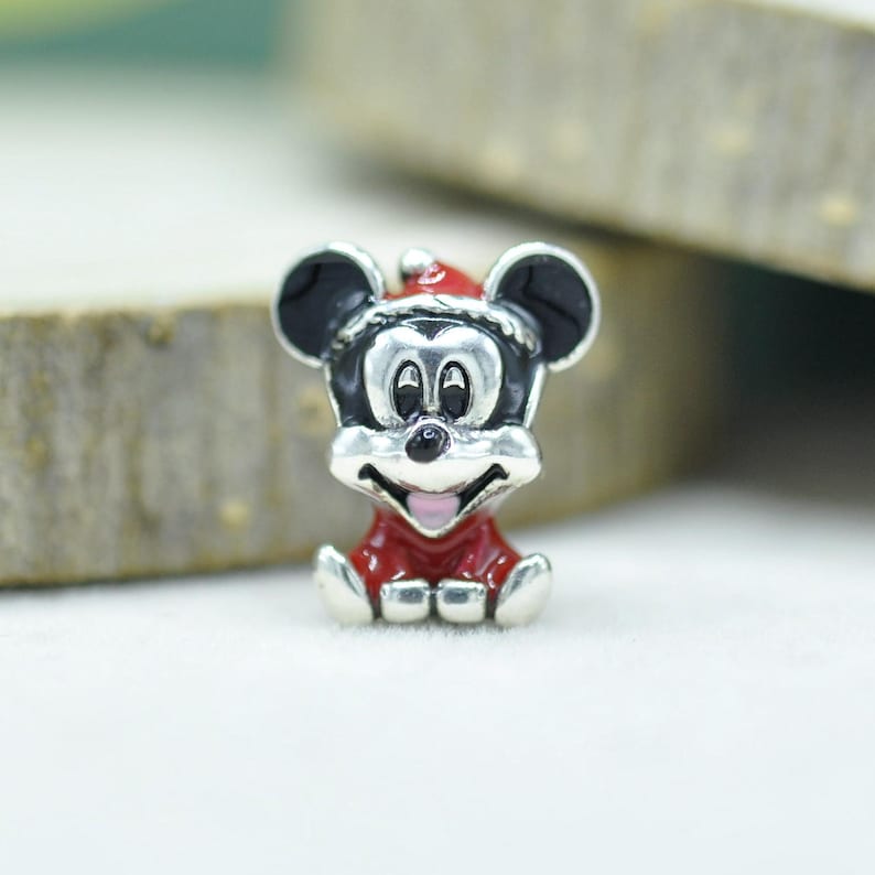 May include: A silver-toned metal charm shaped like a cartoon mouse head wearing a red Santa hat. The design features black enamel on the ears and eyes, a red enamel body, and a small pink accent on the open mouth, creating a festive holiday character.