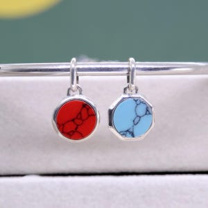 May include: A pair of silver earrings with colorful stone pendants. One earring features a round red stone, while the other has a light blue, octagonal stone. The stones have a marbled appearance.