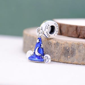 May include: A silver charm with a blue wizard hat design, featuring a crescent moon and stars. The charm is attached to a silver bead with the inscription "ALE S925 PANDORA". The hat has a glossy finish.