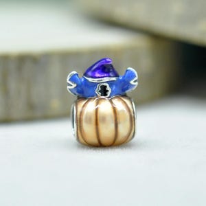 May include: A metal charm bead shaped like a pumpkin with a glossy tan finish and vertical ridges. The pumpkin is topped with a blue enamel wizard hat featuring a dark purple pointed tip and silver-toned trim around the brim and base.