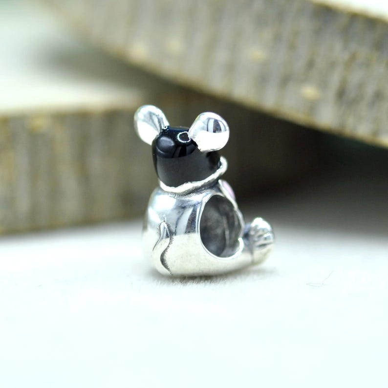 Puede incluir: Un abalorio de plata con forma de peque&ntilde;o animal con cabeza negra y orejas grandes. El cuerpo es de plata pulida con un centro hueco, un detalle de cola peque&ntilde;a y un pie visible. El dise&ntilde;o presenta un acabado met&aacute;lico liso y brillante.