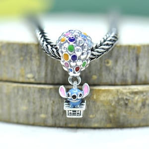 May include: A silver charm bead featuring a hot air balloon with colorful enamel dots, attached to a dangling silver basket containing a small blue character with large ears, designed to slide onto a bracelet chain.