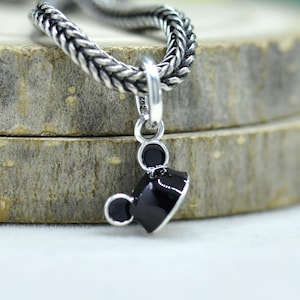 May include: A silver charm with a black graduation cap design. The charm is attached to a silver chain. The cap has a shiny black finish and a small silver accent. The charm is likely a pendant for a necklace or bracelet.
