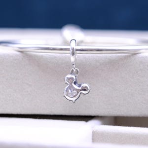 May include: Silver charm in the shape of Mickey Mouse's head, hanging from a silver bracelet.