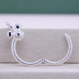 Pu&ograve; includere: Un braccialetto color argento con un design ispirato a Mickey Mouse. Il braccialetto presenta un ciondolo a forma di cuore e una fascia a spirale. Il ciondolo ha due piccole orecchie rotonde e un viso a forma di cuore. Il braccialetto &egrave; in metallo lucido.