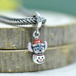 Puede incluir: Un charm de plata que muestra un personaje con orejas grandes y un gorro de Pap&aacute; Noel rojo y blanco, unido a un cuerpo de mu&ntilde;eco de nieve con nariz naranja y bufanda roja. El charm tiene grabado el nombre Pandora y cuelga de una cadena.