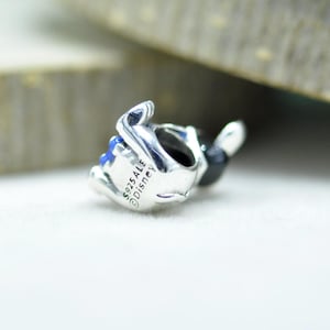 Puede incluir: Un charm de plata pulida con un dise&ntilde;o de personaje y detalles en esmalte negro y azul. El lateral del charm est&aacute; grabado con el texto S925 ALE y Disney, lo que indica la composici&oacute;n de plata de ley y la colaboraci&oacute;n de la marca.