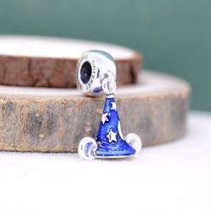 May include: A silver charm with a blue wizard hat design. The hat is dark blue with white stars and a white trim. The charm has the word "Disney" on it.
