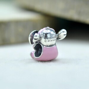 May include: A silver charm bead shaped like a character with large ears and a pink enameled body. The back of the head features engraved text reading S925 ALE and Disney. The charm has a hollow center for threading onto a bracelet or necklace chain.