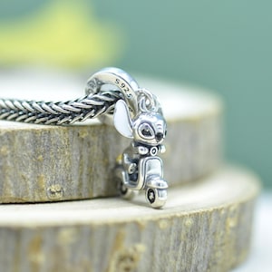 Pu&ograve; includere: Un ciondolo in argento sterling raffigurante un personaggio su uno scooter, con accenti in smalto bianco sulle orecchie. Il ciondolo &egrave; inciso con S925 ed &egrave; fissato a una catena in argento intrecciata, con lavorazione in metallo dettagliata.