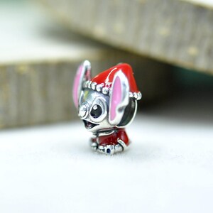 Puede incluir: Un abalorio de plata con forma de personaje de orejas grandes, que lleva un gorro de Pap&aacute; Noel rojo con borde blanco y un conjunto rojo a juego. El personaje presenta orejas rosadas, ojos negros y una nariz peque&ntilde;a con detalles en esmalte.