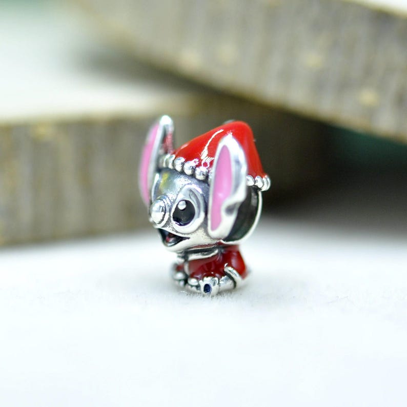 Puede incluir: Un abalorio de plata con forma de personaje de orejas grandes, que lleva un gorro de Pap&aacute; Noel rojo con borde blanco y un conjunto rojo a juego. El personaje presenta orejas rosadas, ojos negros y una nariz peque&ntilde;a con detalles en esmalte.