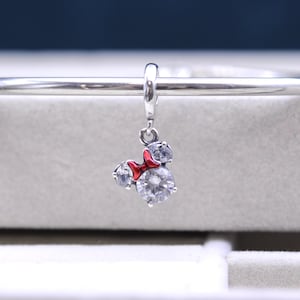 May include: Silver charm with a red bow and clear crystal accents in the shape of Mickey Mouse's head.