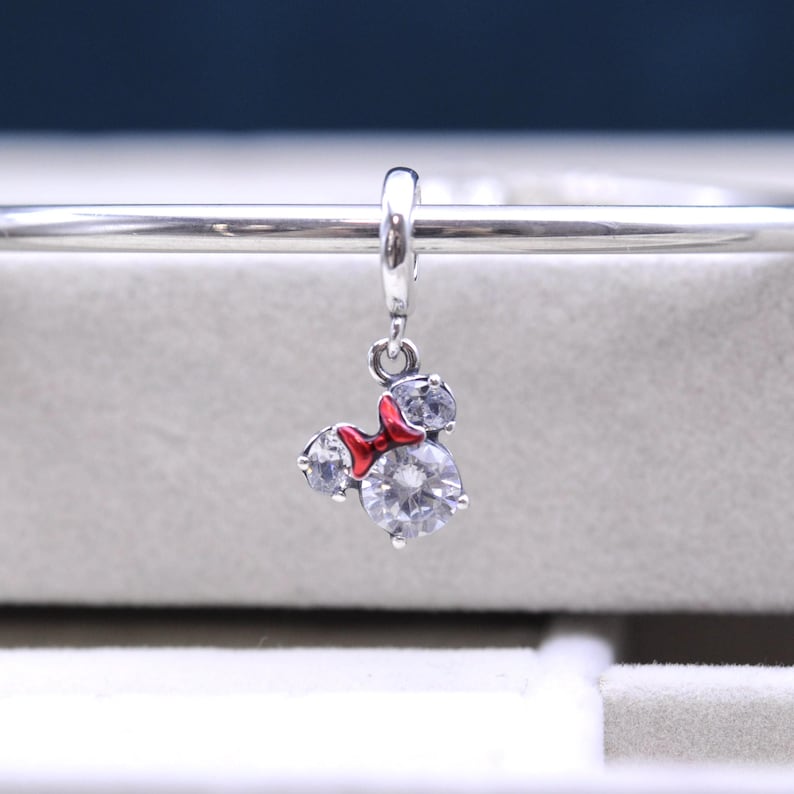 May include: Silver charm with a red bow and clear crystal accents in the shape of Mickey Mouse's head.
