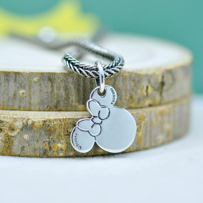 Peut inclure: Un collier avec un pendentif argent&eacute; repr&eacute;sentant la t&ecirc;te de Mickey Mouse avec un n&oelig;ud. Le pendentif est attach&eacute; &agrave; une cha&icirc;ne tress&eacute;e. Le pendentif porte l'inscription "Pandora".