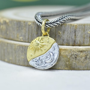 Può includere: Collana con pendente in oro e argento con design sole e luna. Il pendente rotondo presenta un sole dorato su una metà e una luna e stelle argentate sull'altra. La collana ha una catena d'argento.