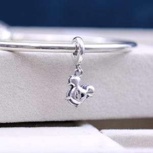 May include: Silver charm in the shape of Mickey Mouse, hanging from a silver bracelet.
